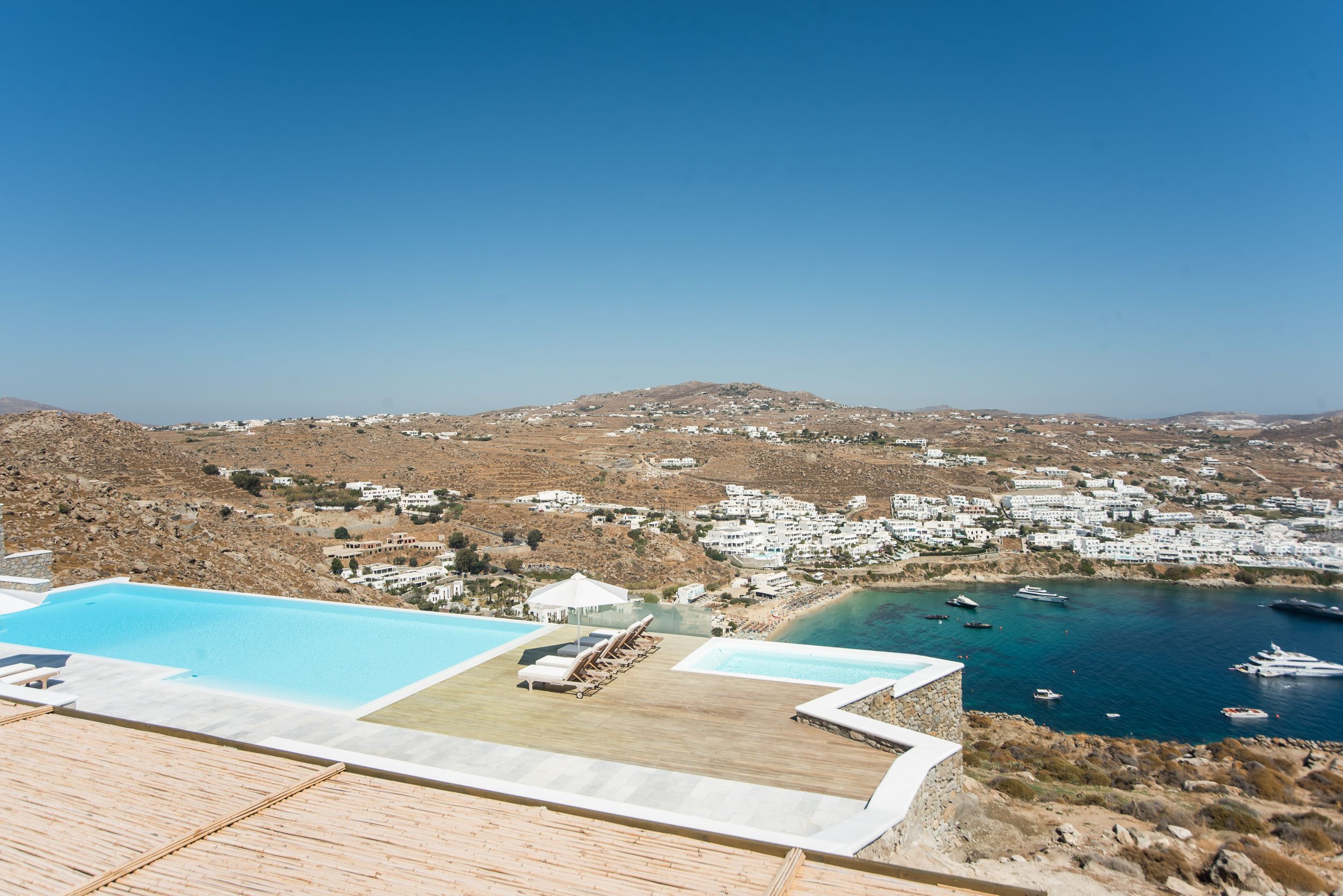Luxury infinity pool overlooking the Mediterranean sea and white buildings of Mykonos, Greece against clear blue sky.