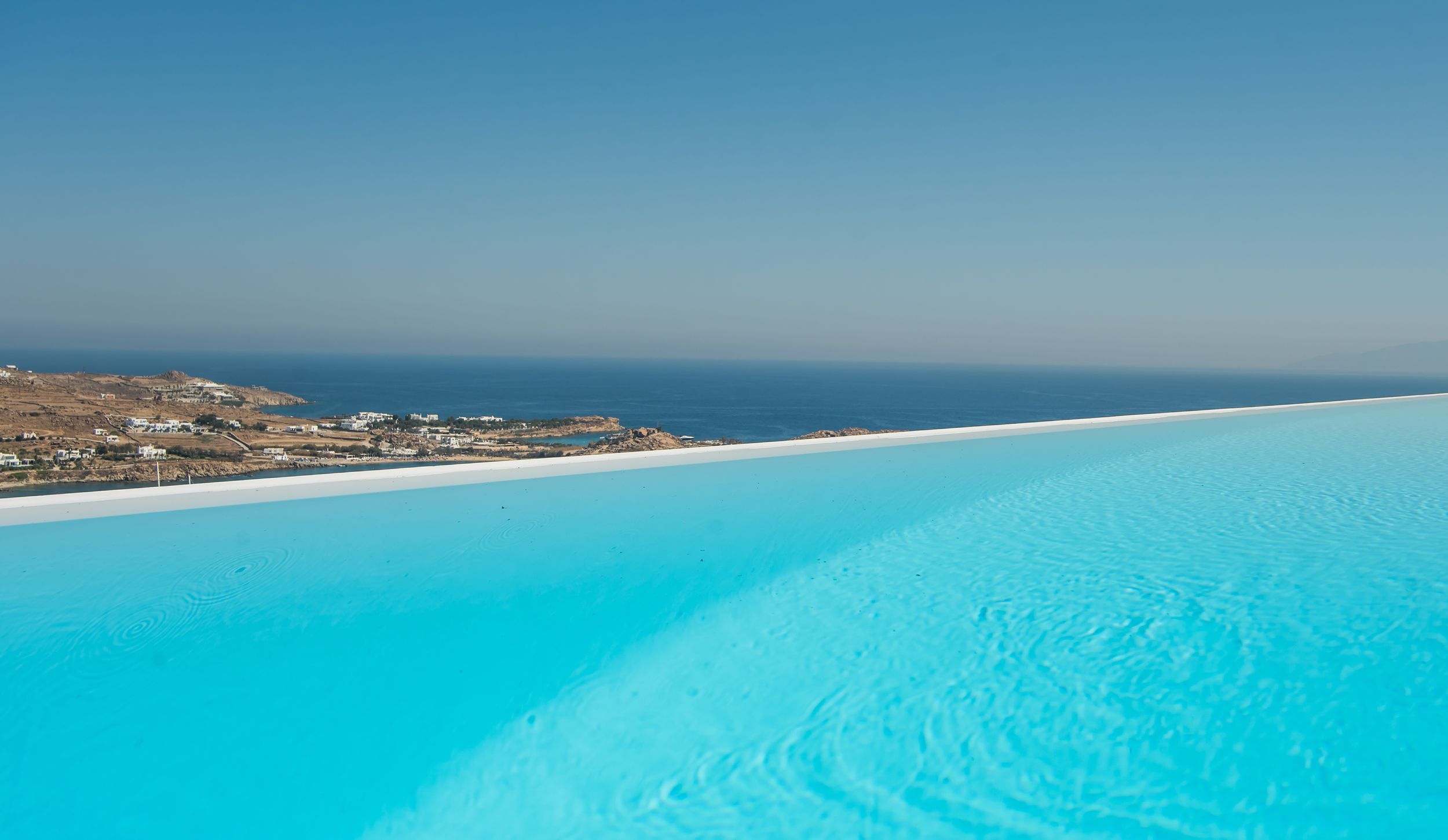 Stunning infinity pool with bright turquoise water overlooking coastal landscape and ocean views against clear blue sky.
