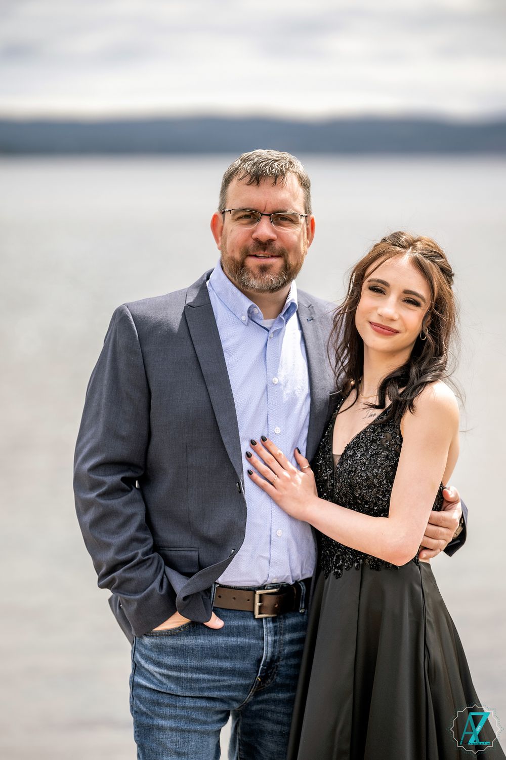 A formal portrait of two people in dressy attire against a lakeside background.