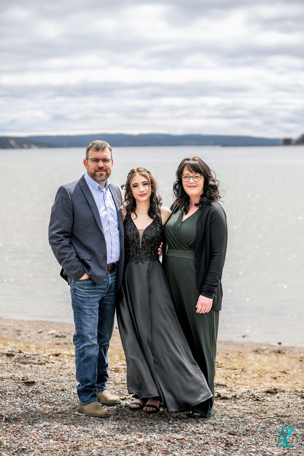 A family portrait on a rocky beach with a lake and cloudy sky in the background.