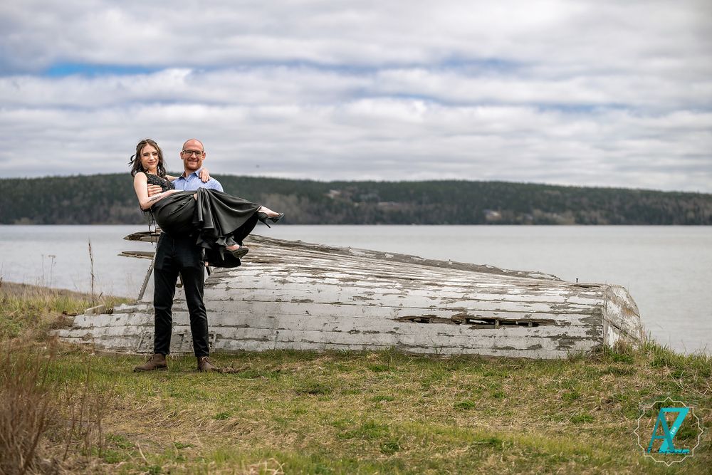 A couple shares a playful moment on a large driftwood log by the water's edge.