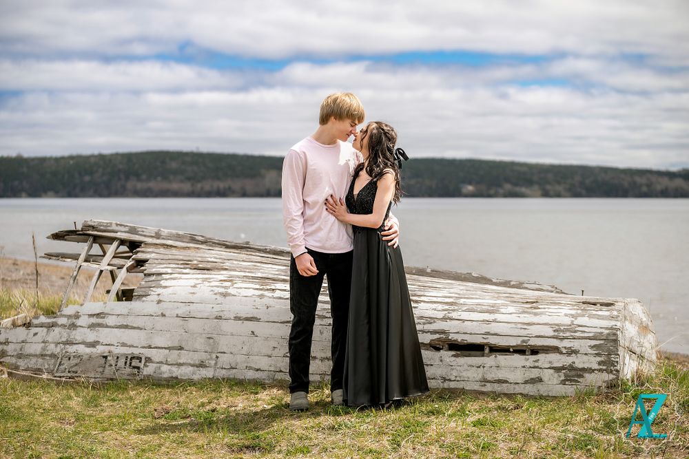 A romantic couple embraces by a weathered driftwood log overlooking a scenic waterfront.
