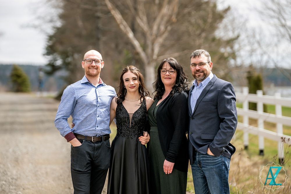 Four people dressed formally pose together on a dirt road lined with white fencing.