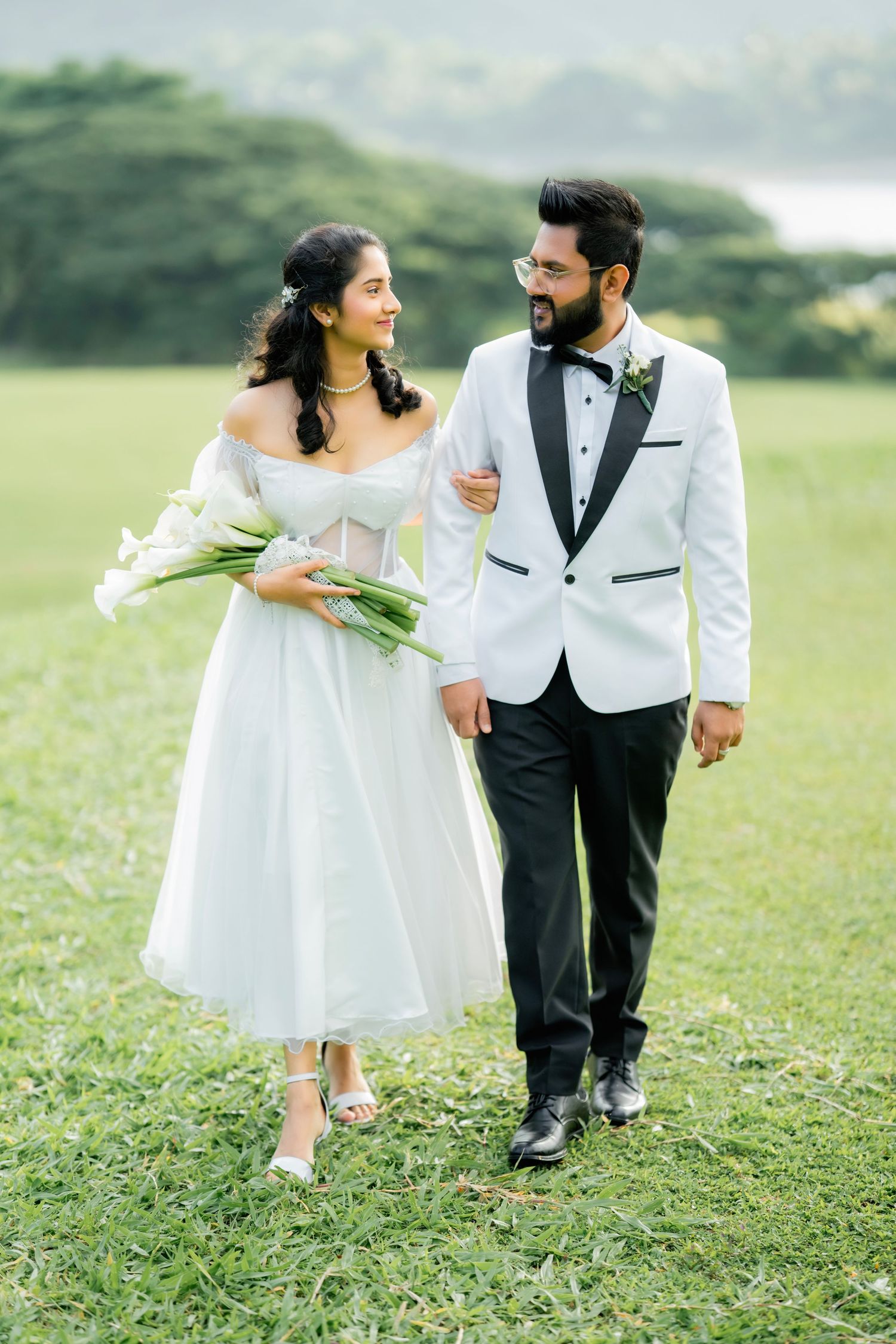 Couple in matching white outfits walk and play together on grassy field during outdoor photoshoot.