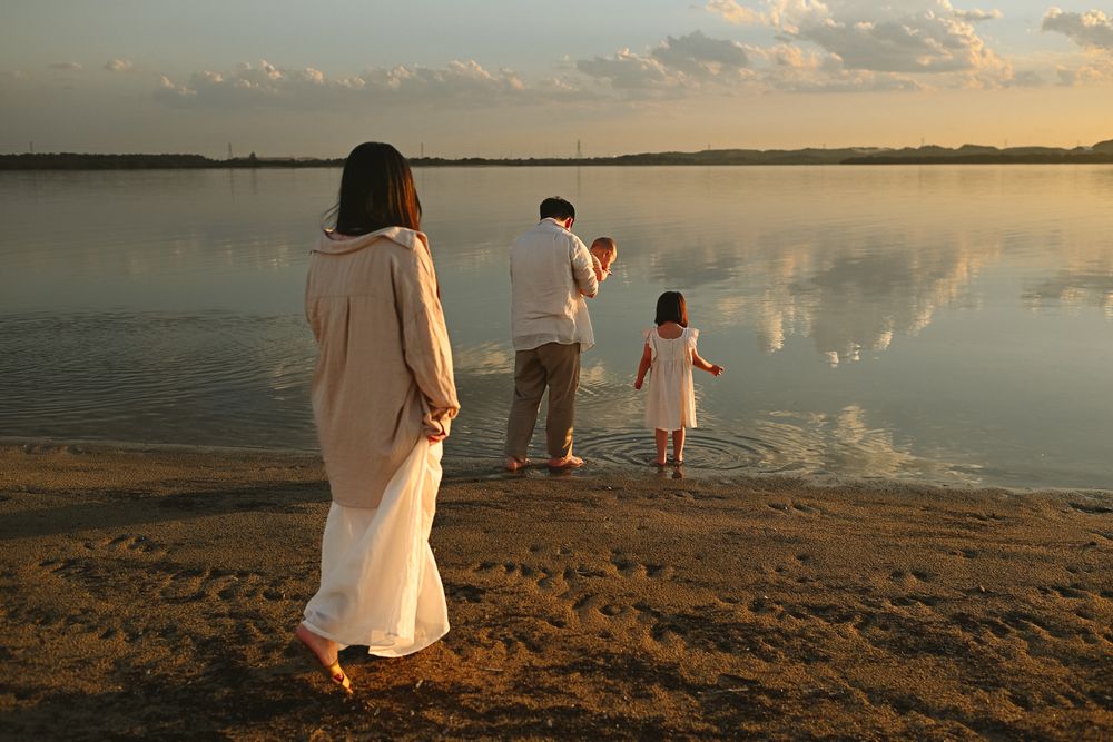 A group in white clothing stands at the beach during a golden sunset, creating silhouettes against the peaceful water.