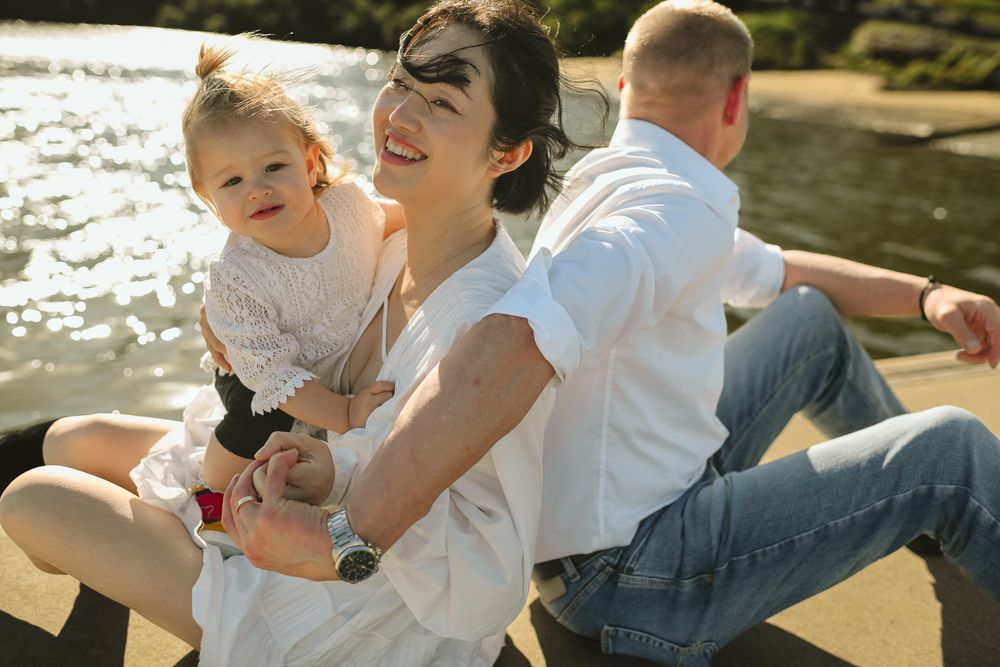 A candid family moment captured at sunset by the water showing joyful laughter and embraces.