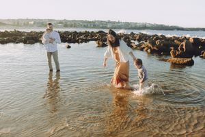 A family plays and splashes in shallow ocean water near rocky shores, on Maroubra beach.