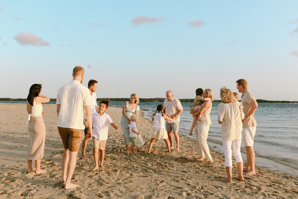 Group of people in light colored clothing gathered at sunset on a beach shoreline.