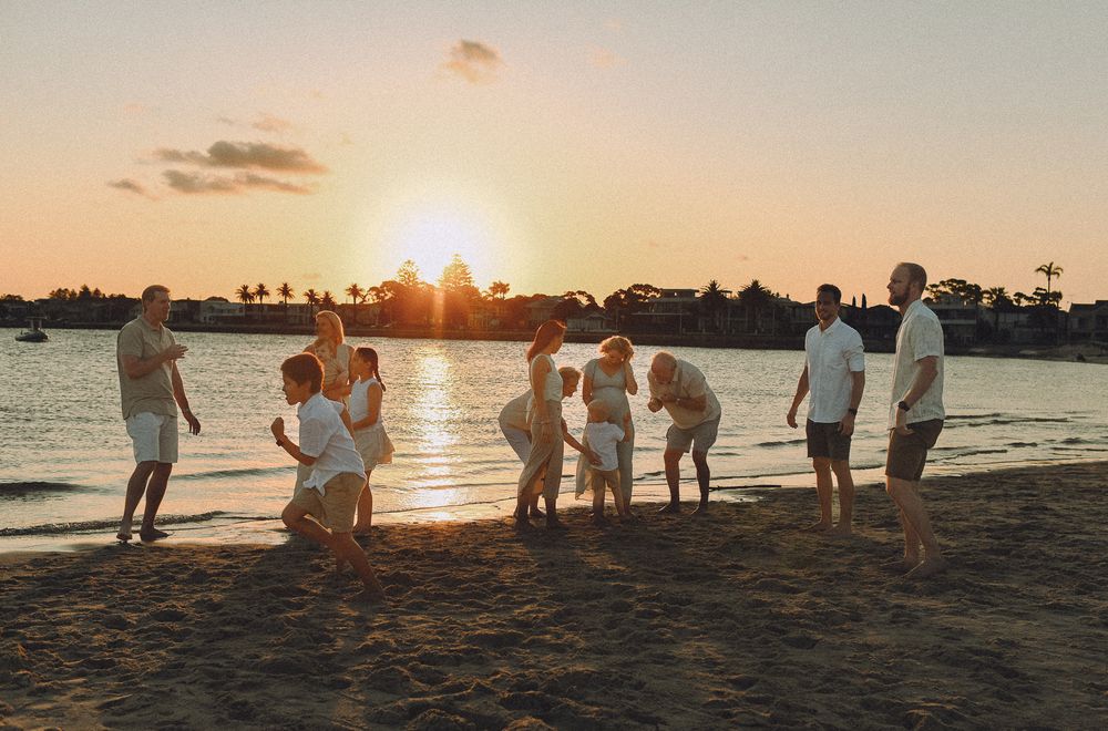 Group silhouettes against golden sunset on beach shore.