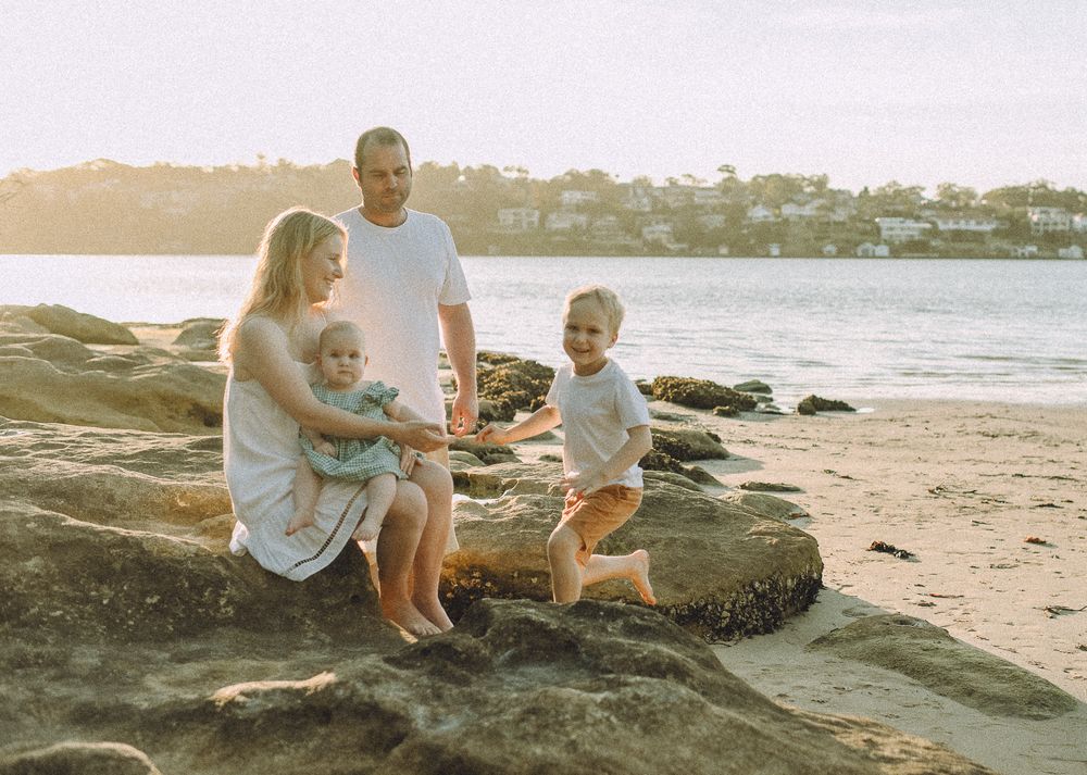 A family sits together on coastal rocks at the beach during golden hour.