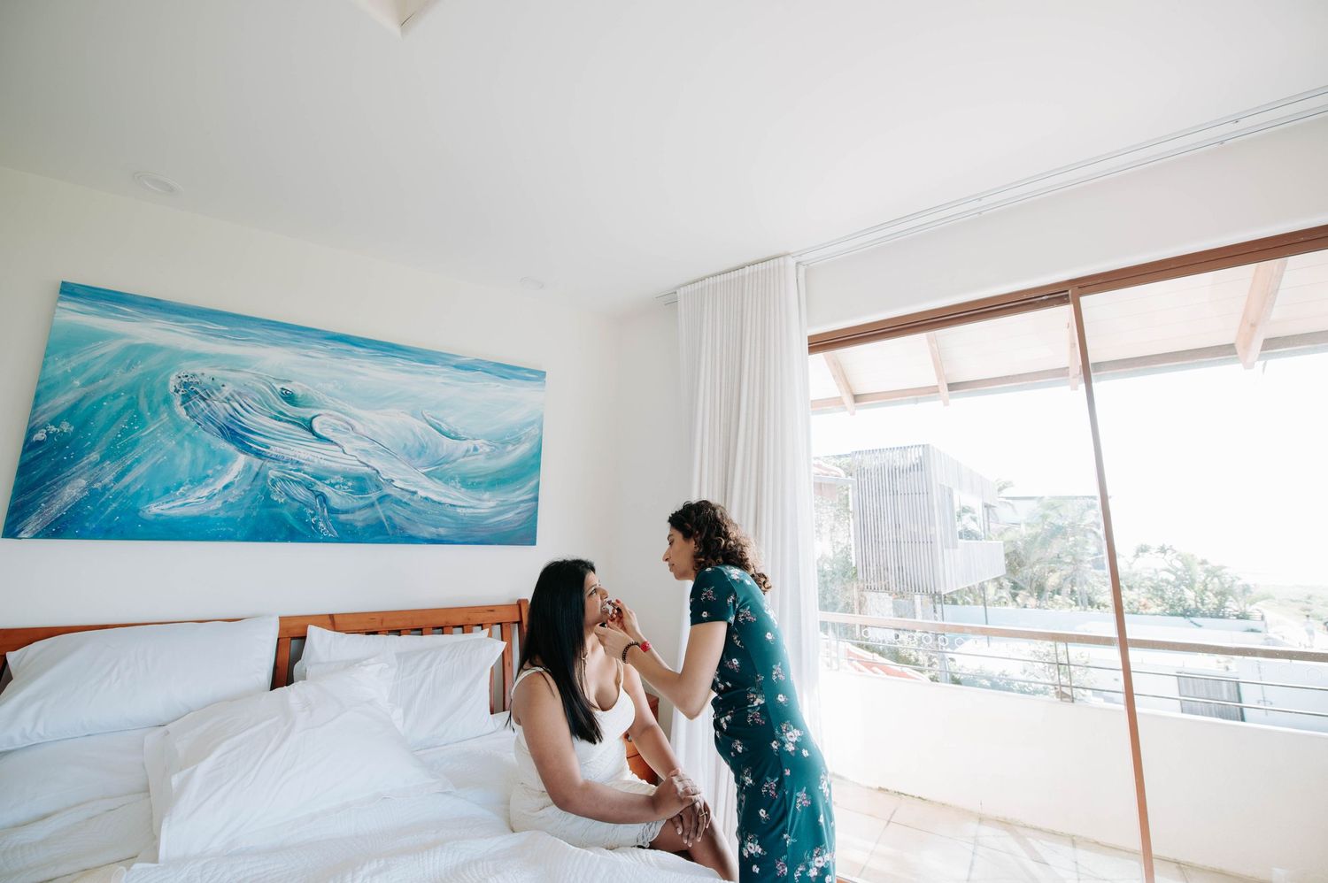 Two people share an intimate moment in a bright bedroom with ocean artwork.