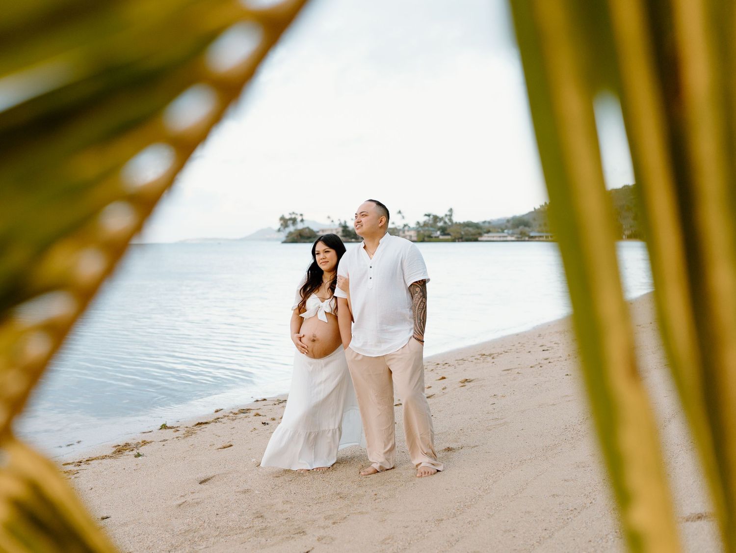A maternity photoshoot with a happy expecting mother and father standing on the beach on Oahu in Hawaii