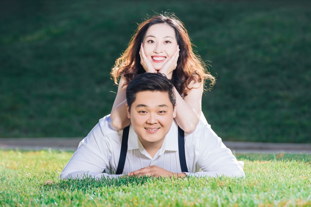 A joyful couple poses playfully on grass in an outdoor portrait session.