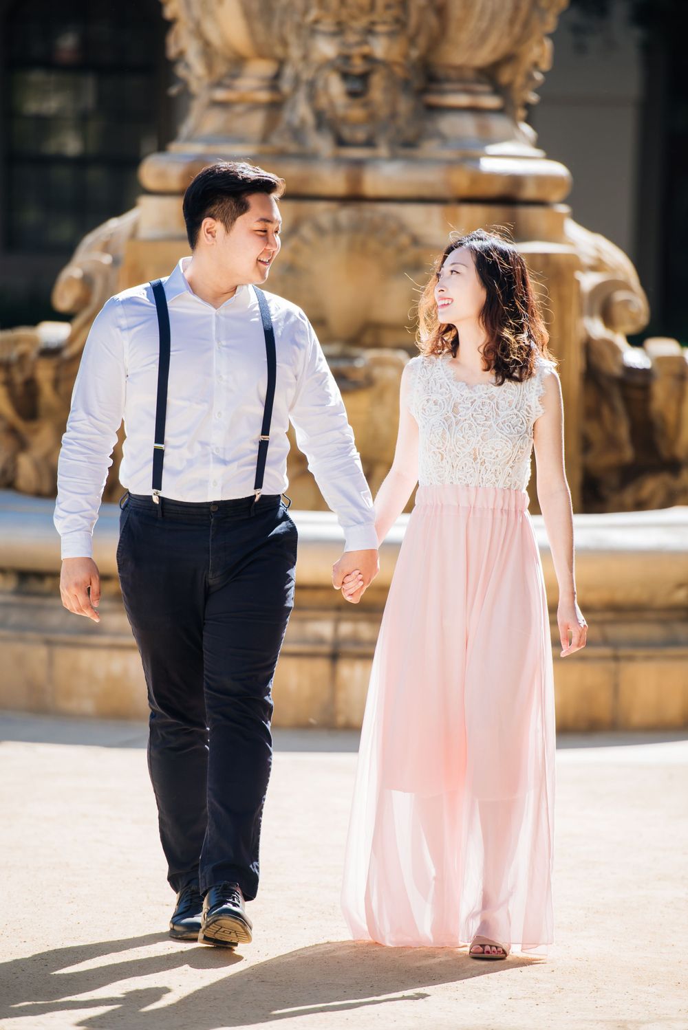 A joyful couple walking hand in hand near an ornate fountain.