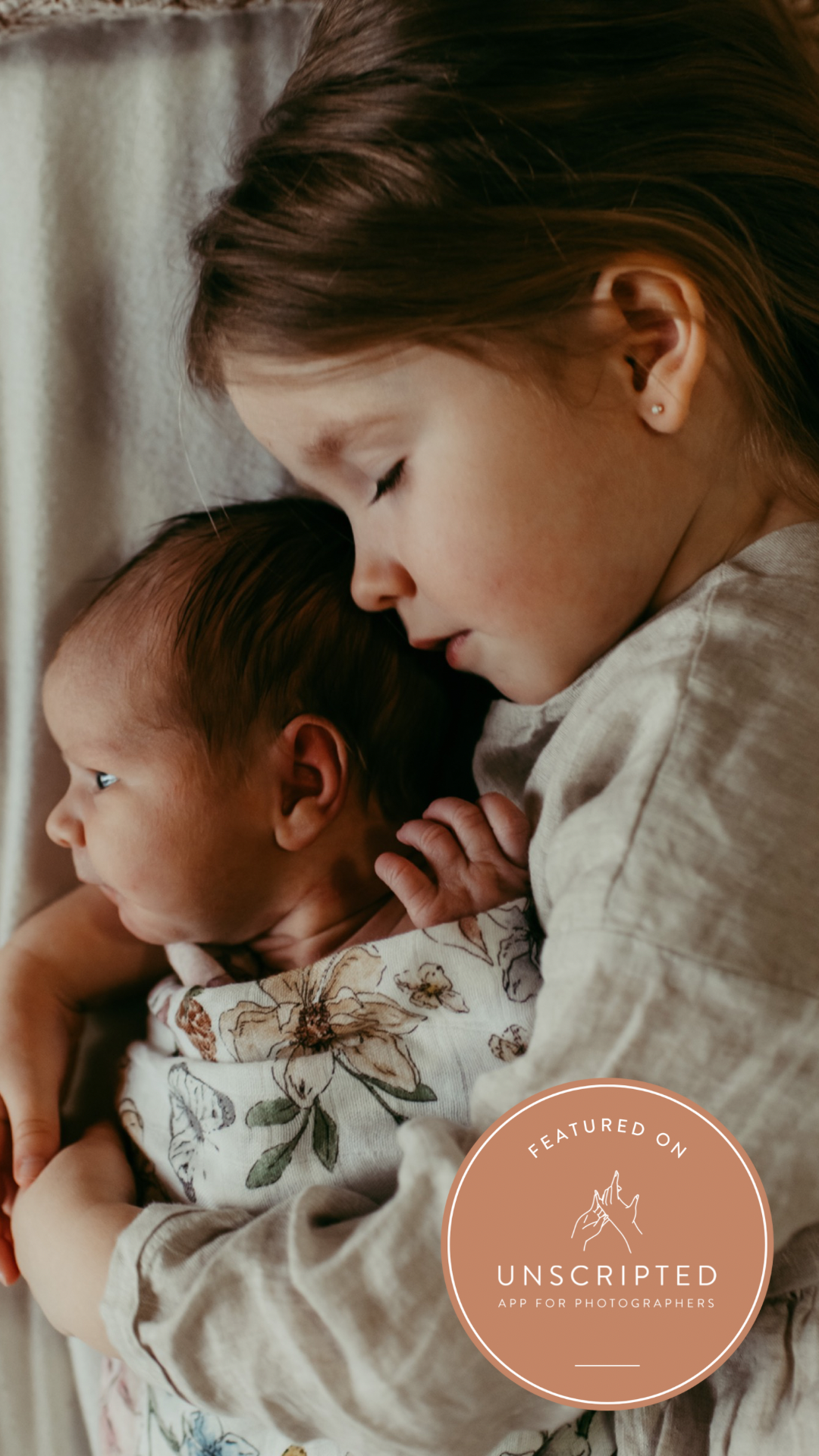 A tender moment captured between siblings as a young child gently embraces a baby in soft lighting.