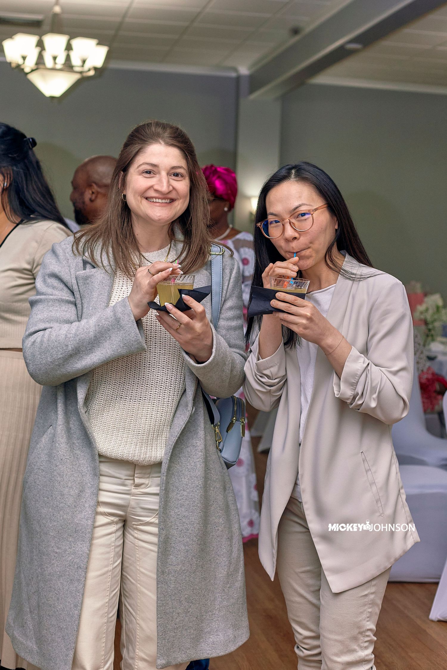 Group of friends in cozy sweaters laughing while looking at their phones in a bright indoor space.