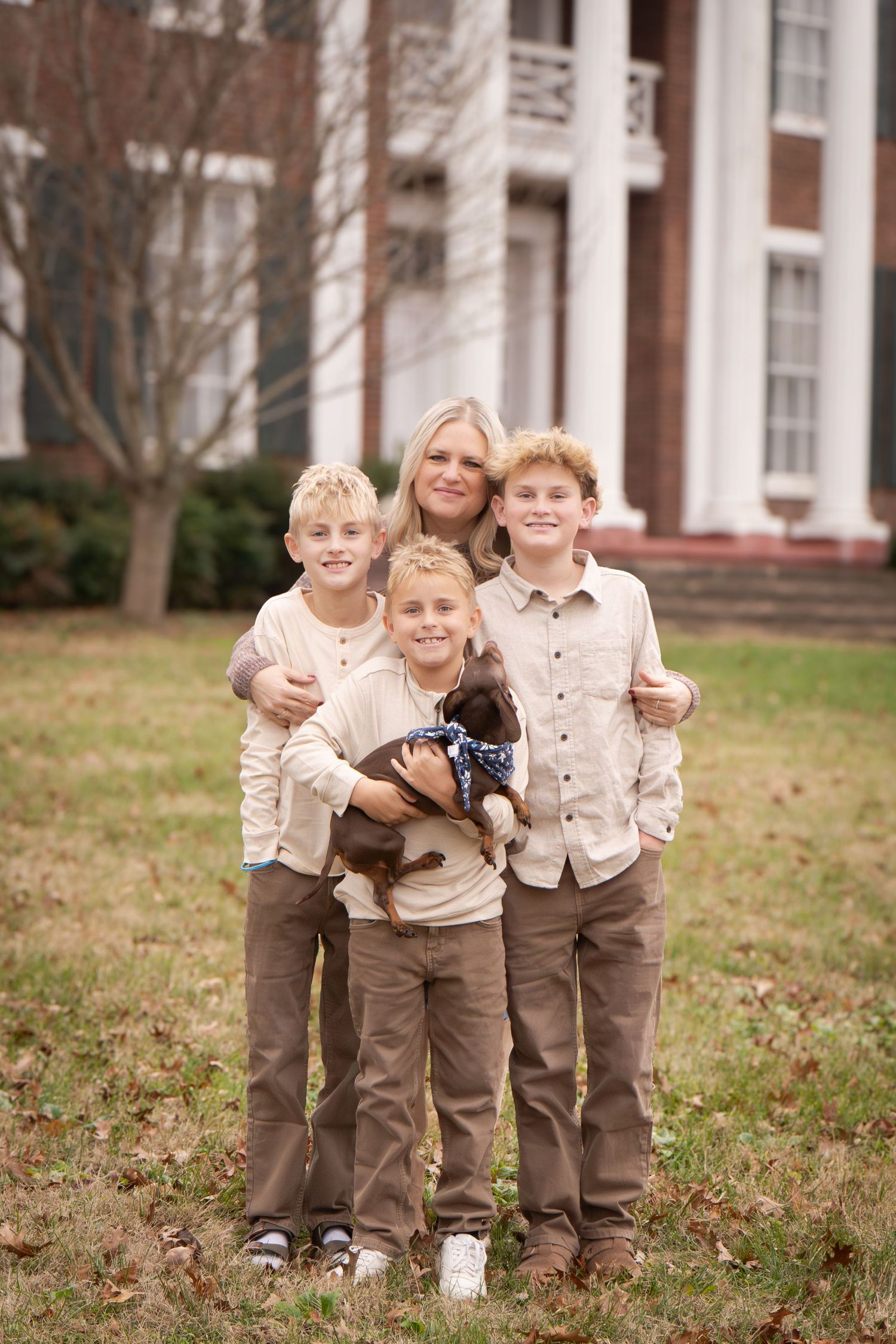 Four young children in matching brown pants and cream shirts play together on a grassy lawn.