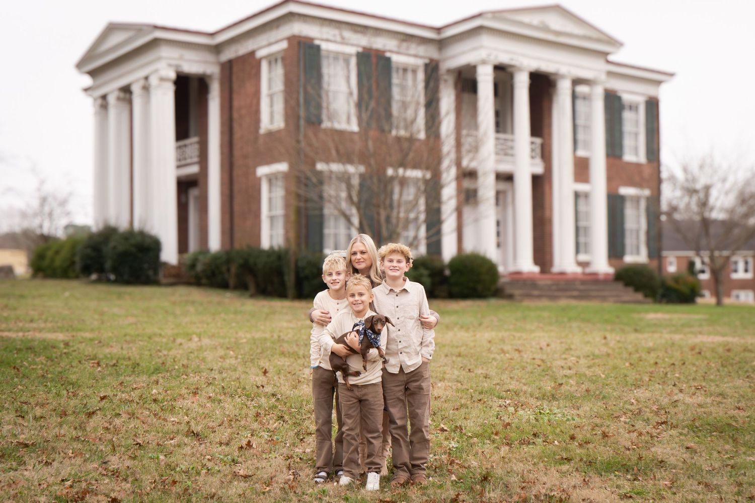 A stately antebellum mansion with tall white columns serves as backdrop for a family portrait on its front lawn.