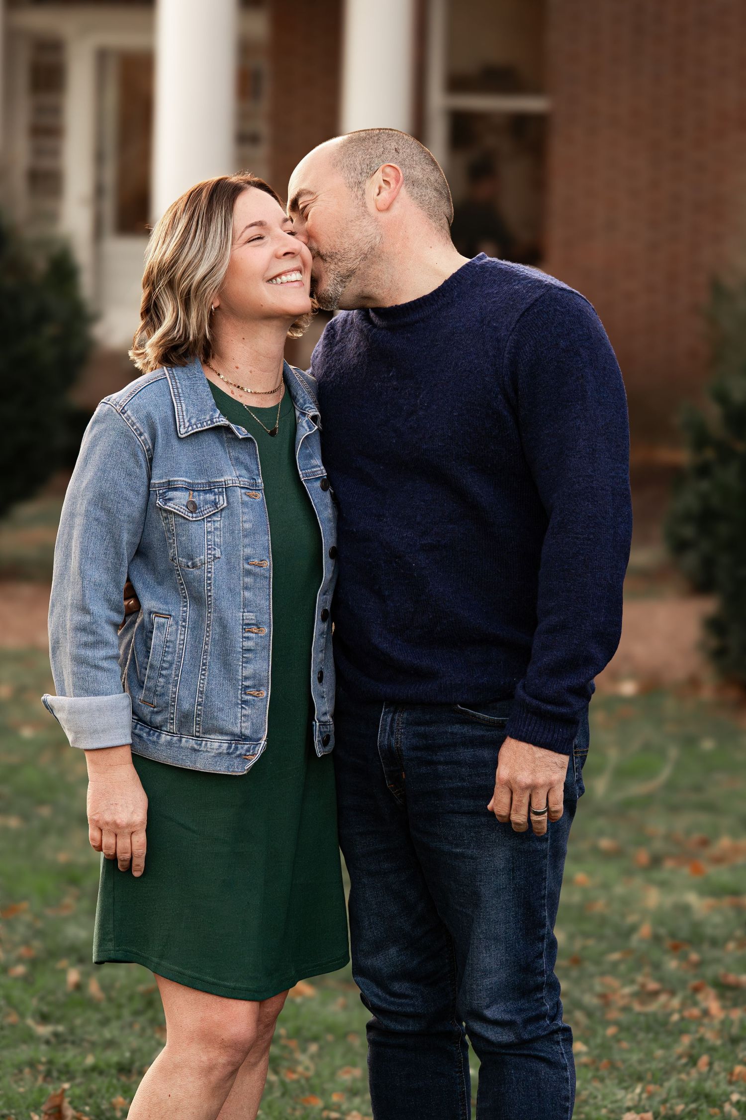 A couple in casual fall attire sharing intimate moments outdoors with fallen leaves in the background.