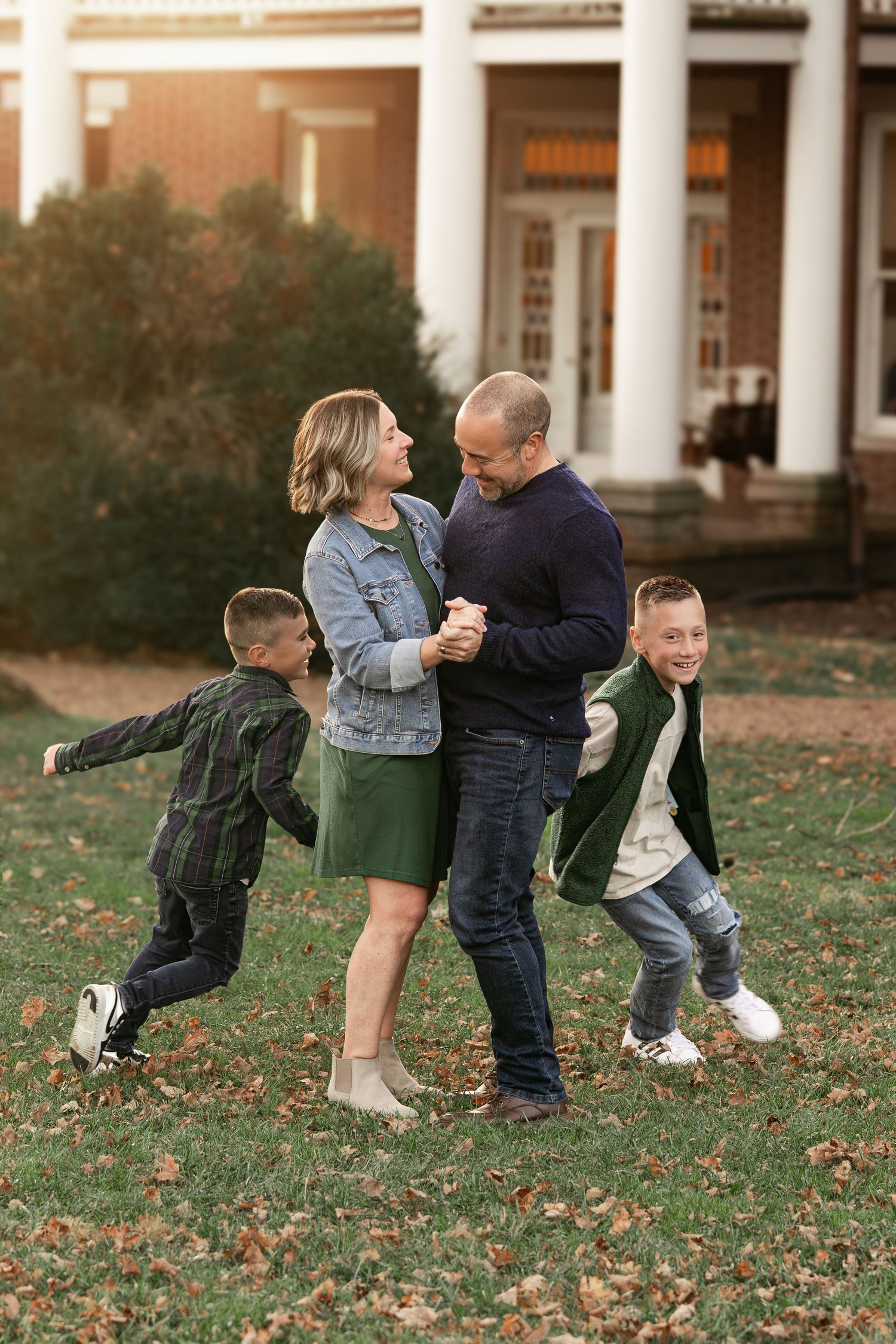 A playful sequence of people dancing and twirling together on a grassy lawn in front of a columned building.