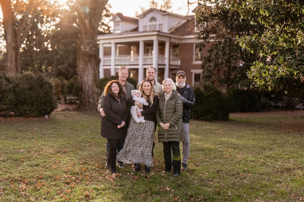 A group stands together in a garden setting during golden hour with autumn trees in the background.