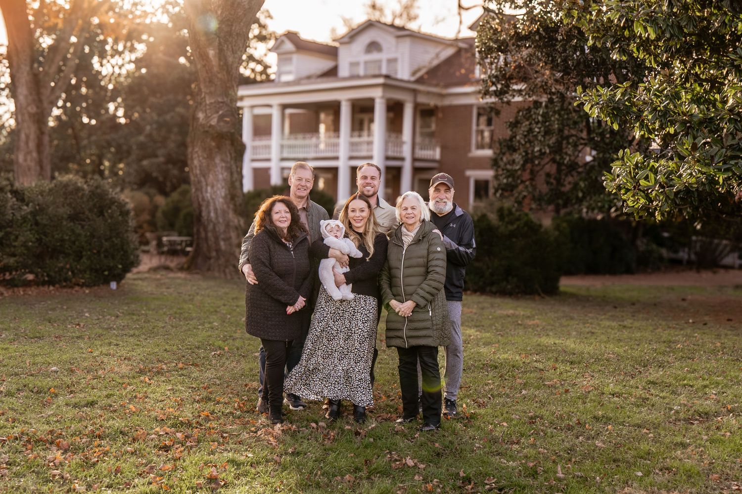 A group stands together in a garden setting during golden hour with autumn trees in the background.