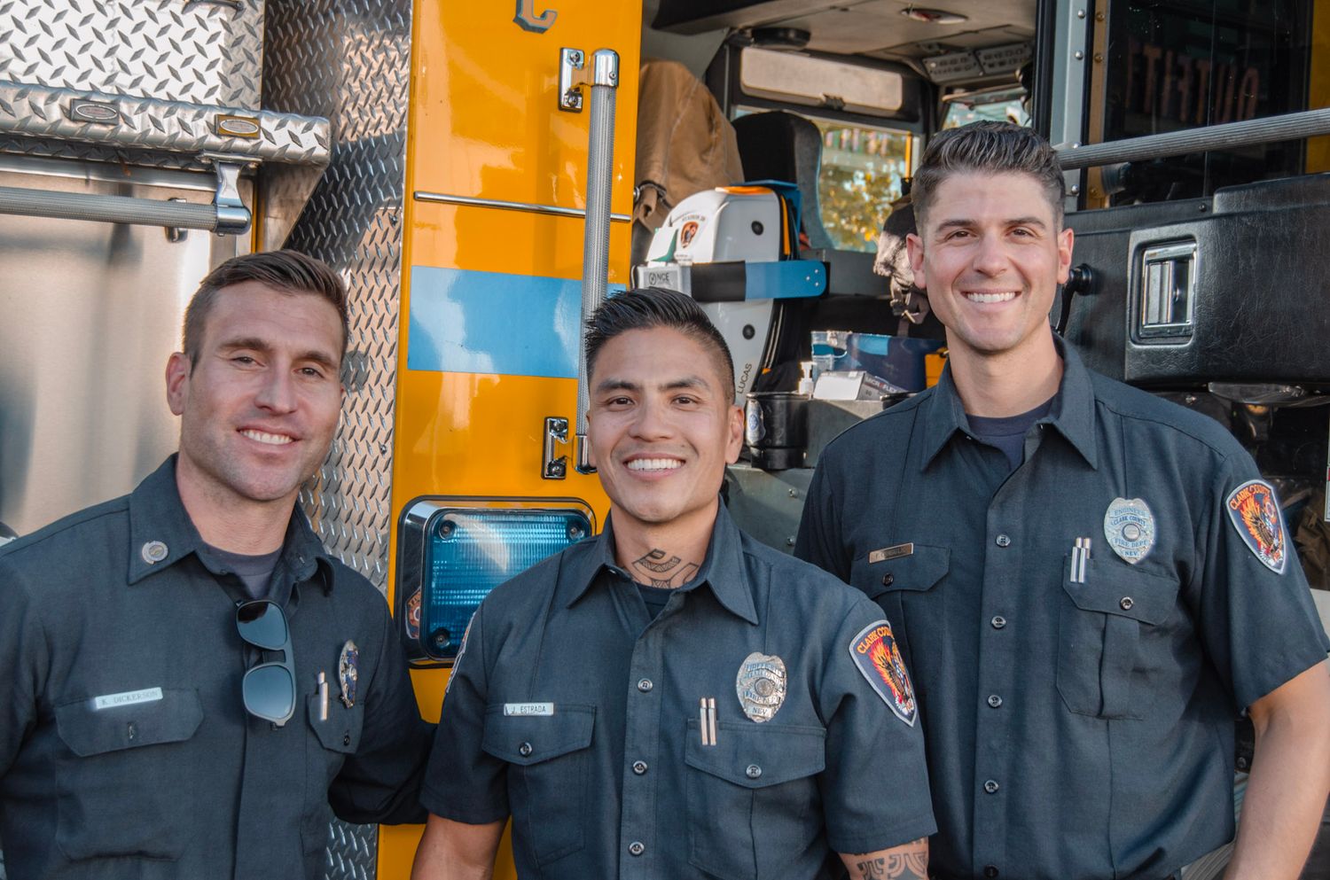 Group of uniformed police officers posing together in front of yellow emergency vehicles.
