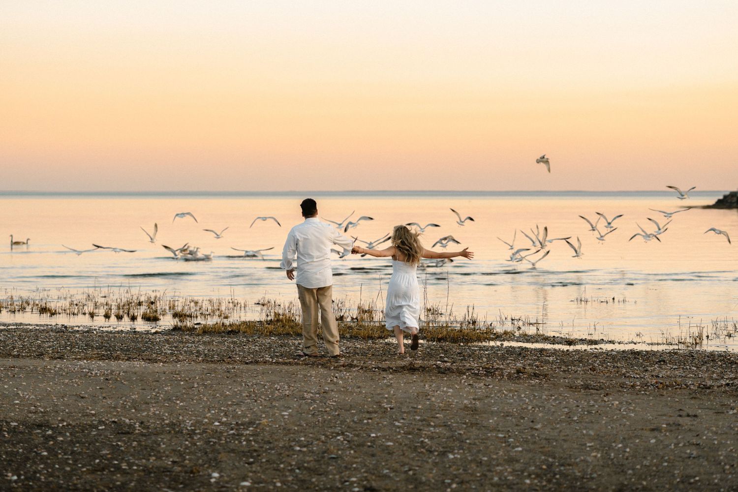 Couple running on the beach towards birds during sunset