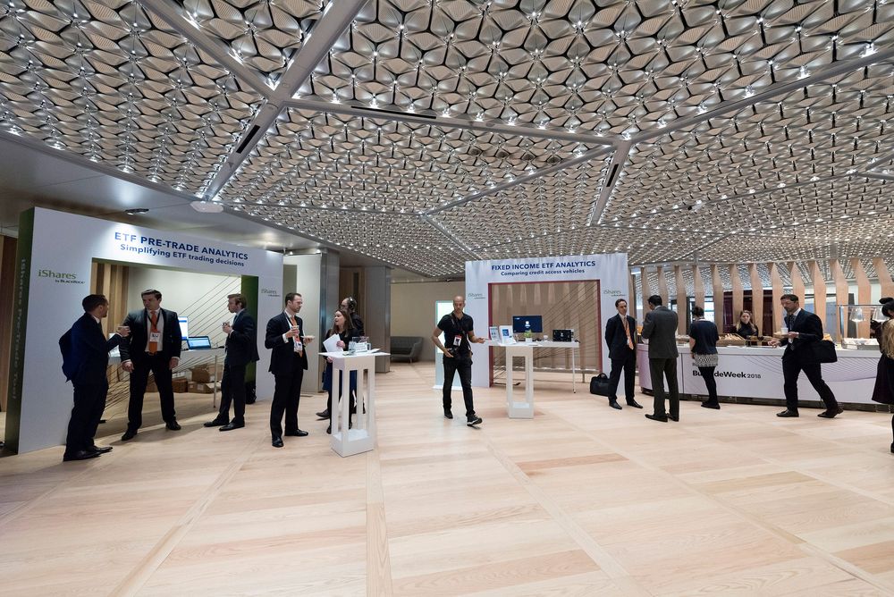 Business professionals networking in a modern conference hall with an ornate geometric ceiling and exhibition displays.