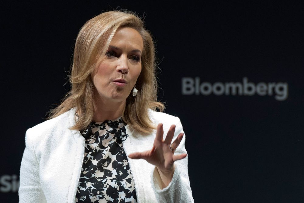 A woman in a white blazer speaks at a Bloomberg conference, gesturing expressively.