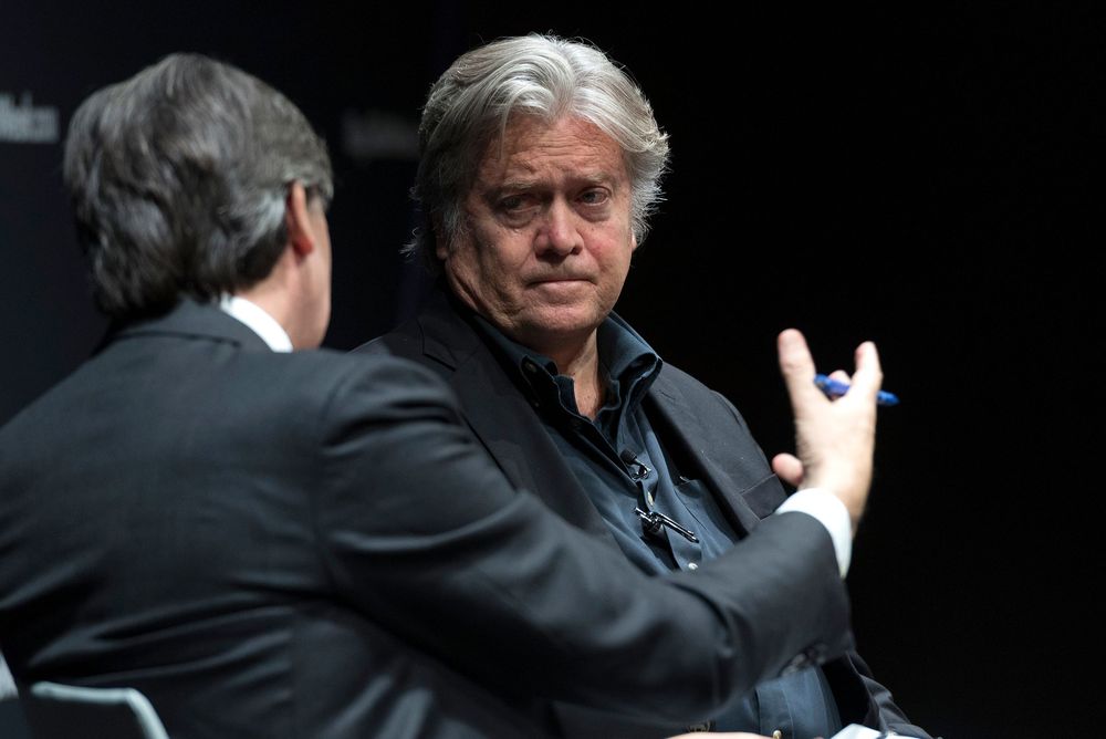 Two men in dark suits engaged in serious conversation at a formal panel event.