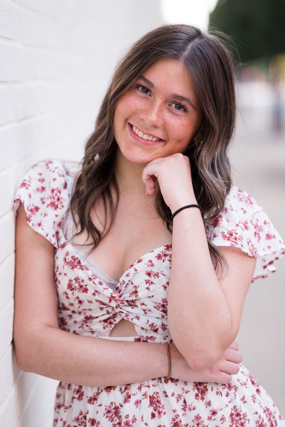 Candid poses in a floral print dress against white architectural background.