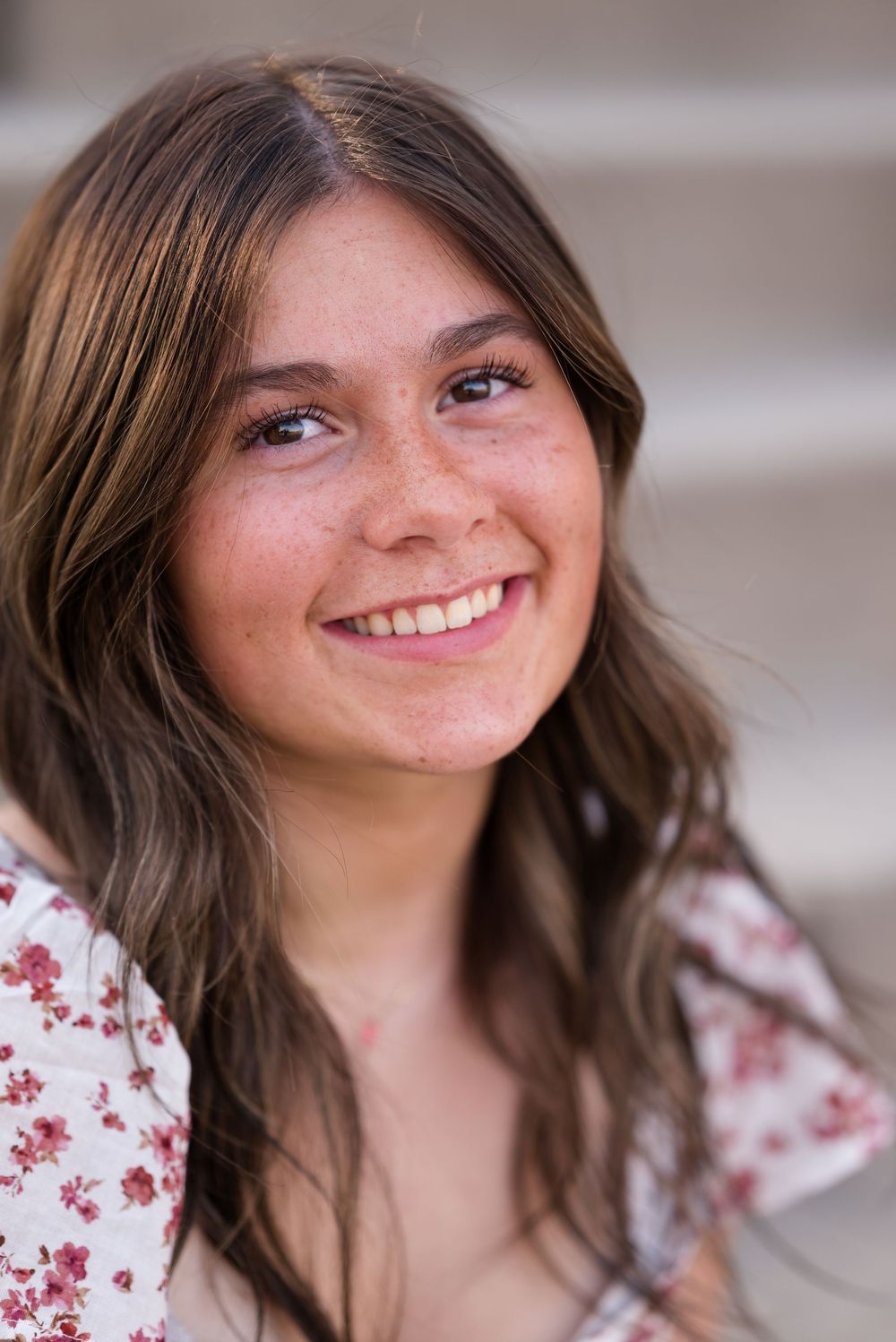Close-up portrait showing natural makeup and wavy brown hair against concrete steps.