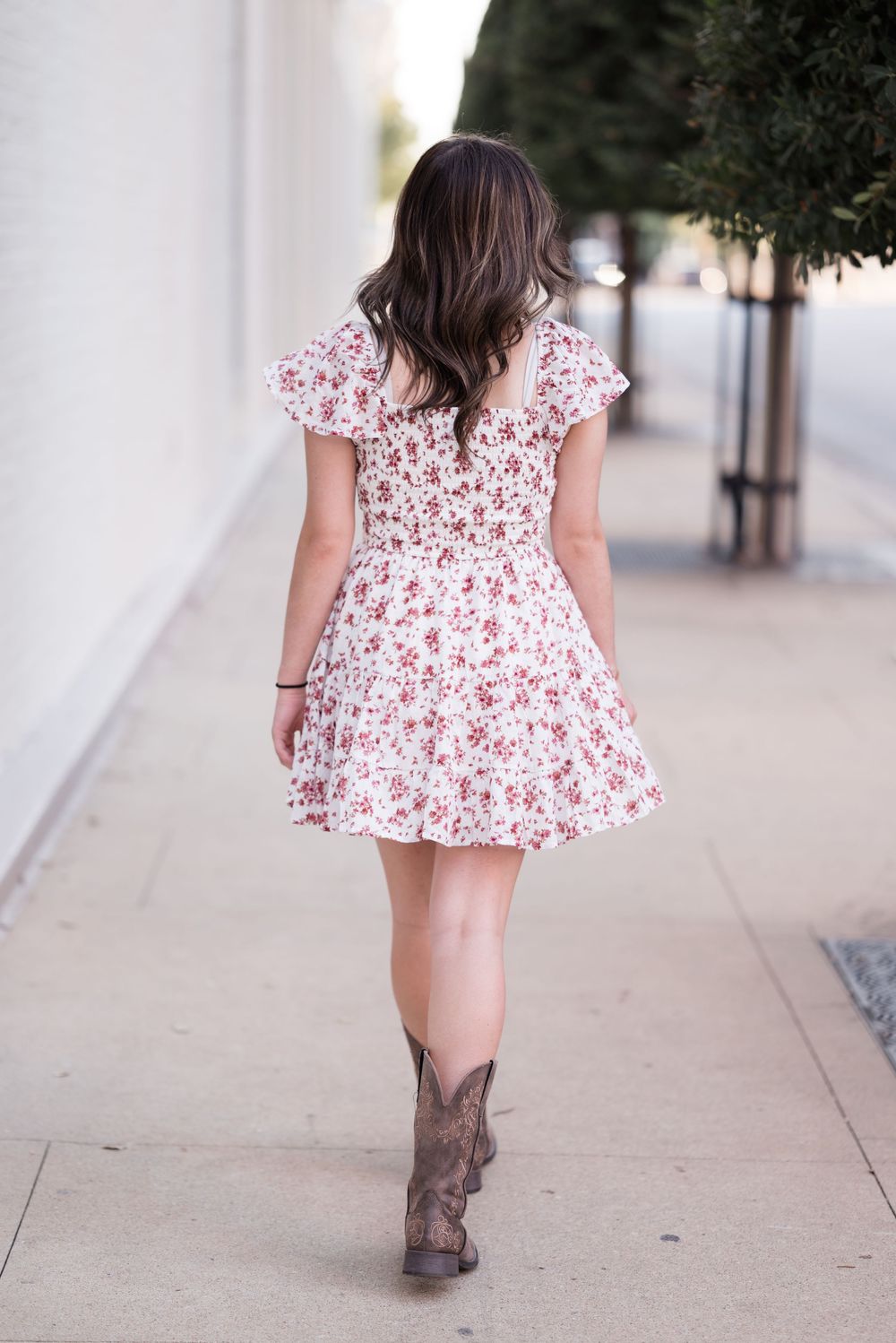 Walking shot from behind showing floral dress and brown boots on concrete path.