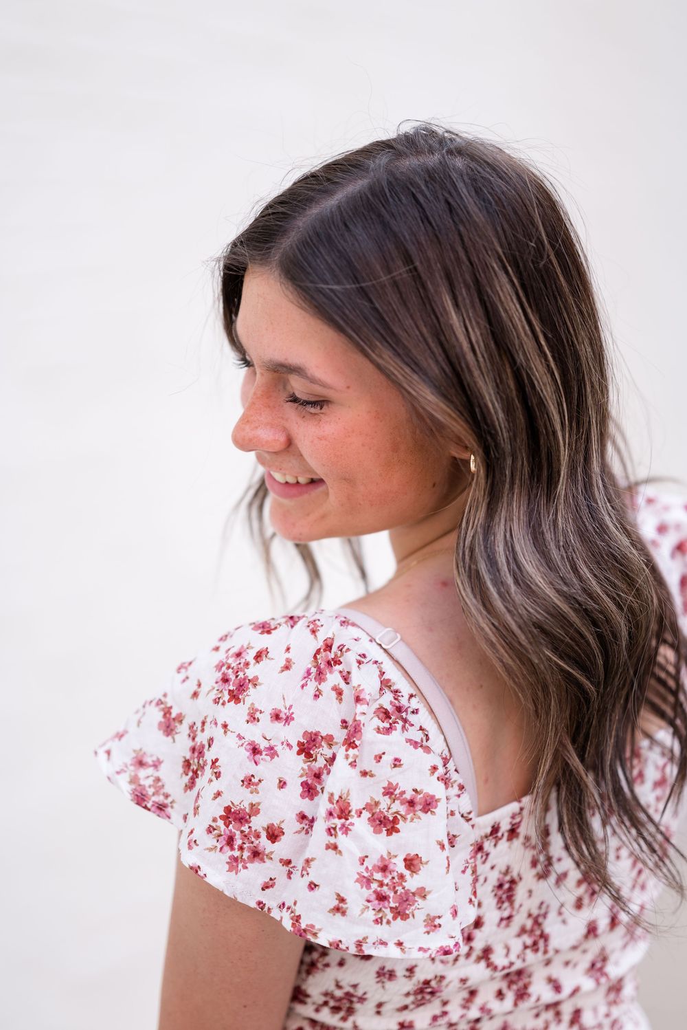 Woman with wavy hair wearing floral print top poses against white background.