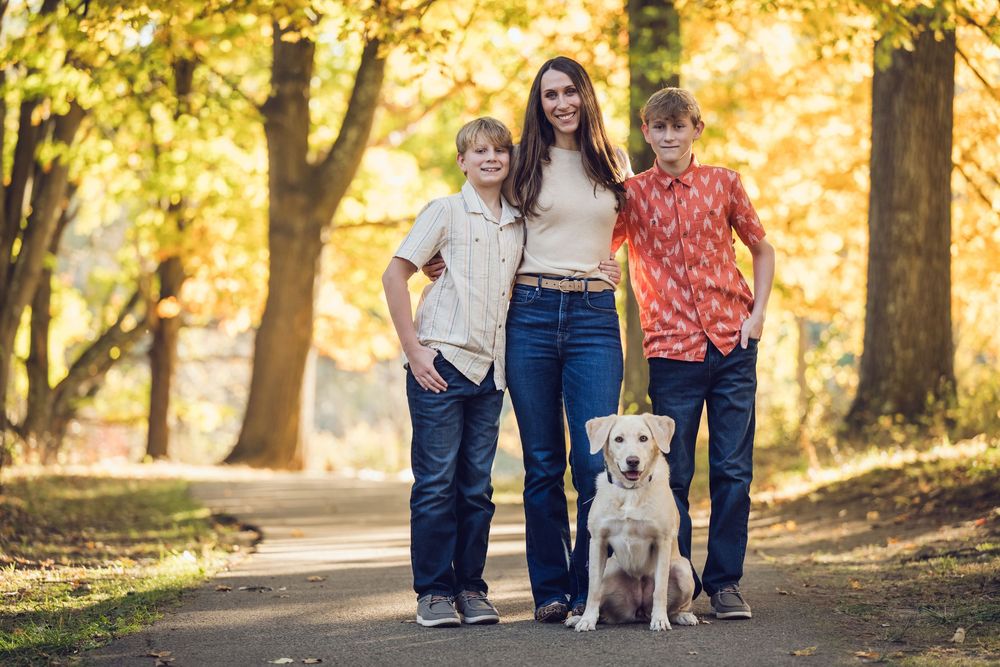 Woman and two boys pose with a yellow Labrador on a tree-lined path during autumn.