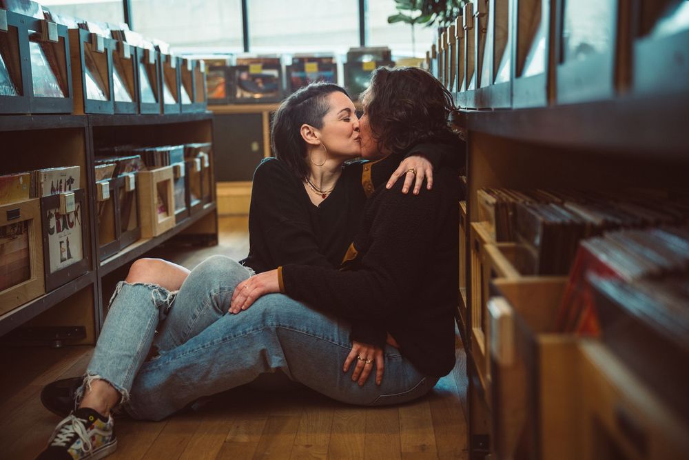 Two people sharing a romantic kiss while sitting on the floor between library bookshelves.