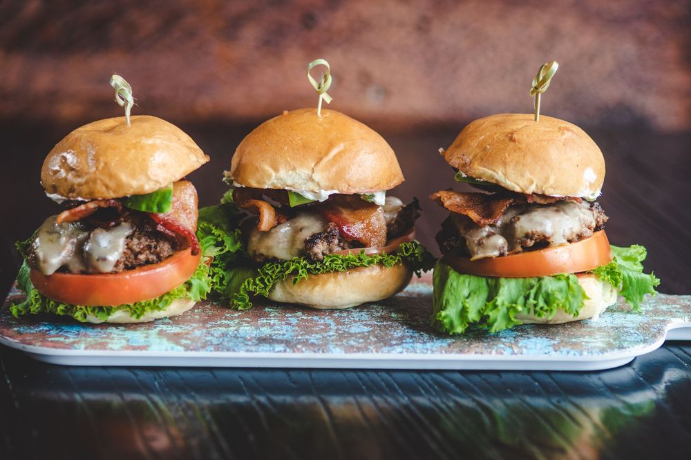 Three gourmet sliders with lettuce, tomato, and mushrooms served on a wooden board.