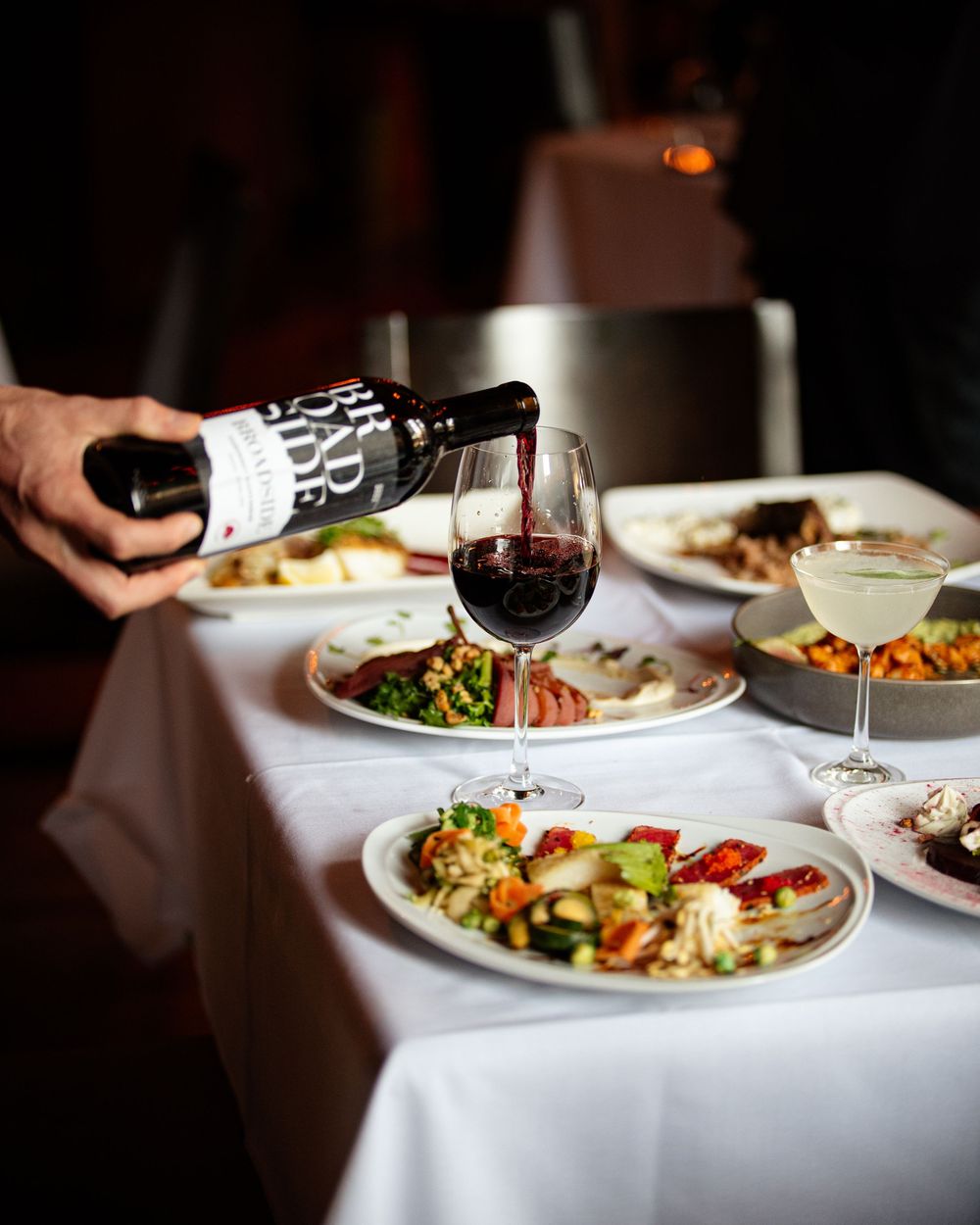 A sommelier pouring red wine at a fine dining table set with multiple gourmet dishes.