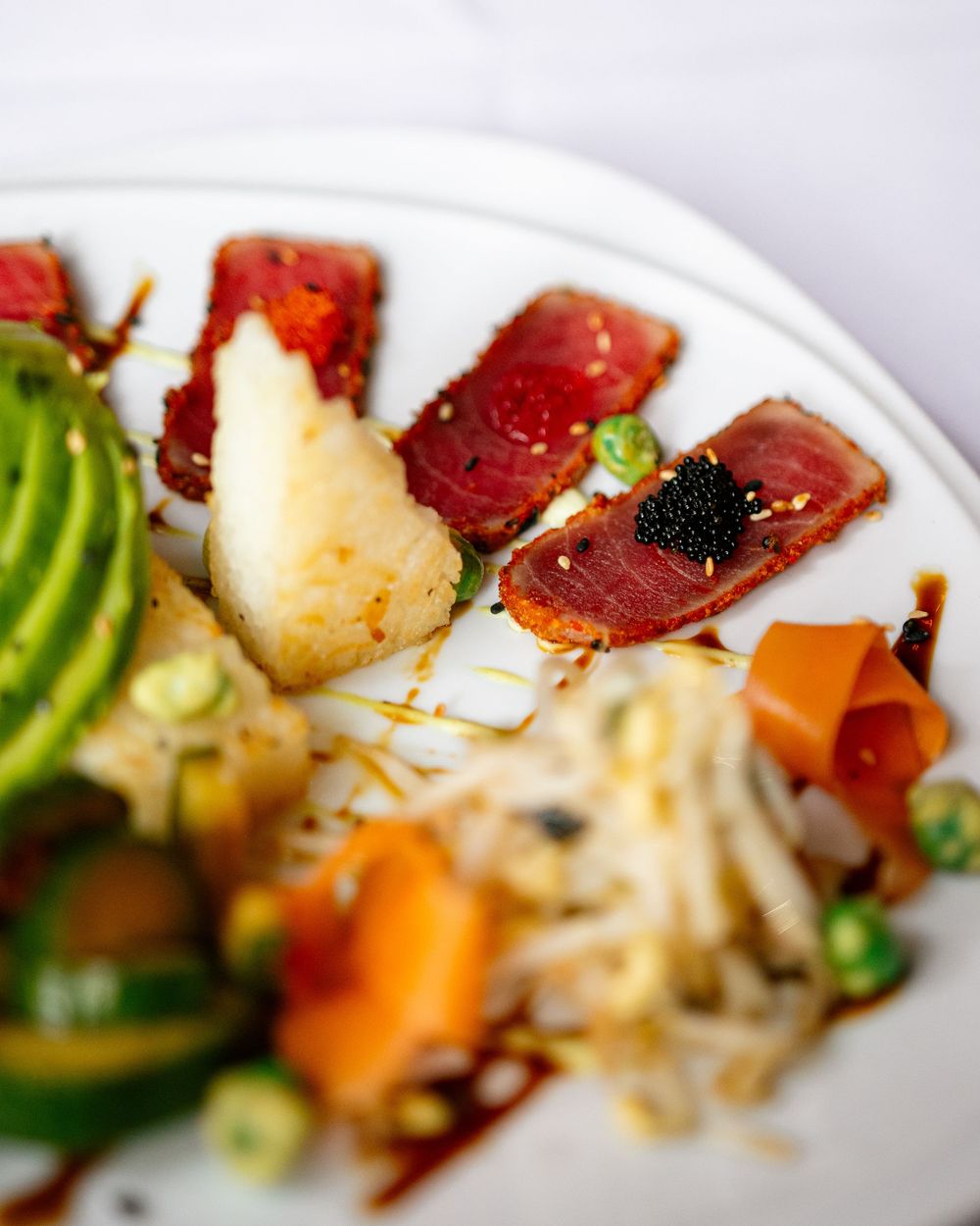A plated tuna sashimi dish with avocado, caviar, papaya, and bean sprouts with soy drizzle.