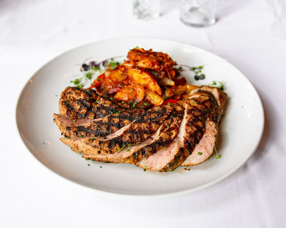 Sliced grilled steak served with roasted tomatoes and herbs on a white plate.