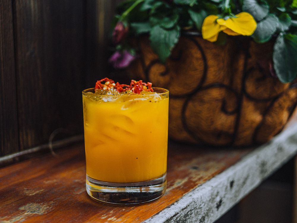 A vibrant golden yellow cocktail garnished with dried flowers in a rocks glass outdoors.