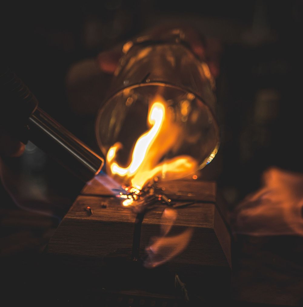 A dramatic flaming cocktail preparation with fire blazing inside a glass on a wooden surface.