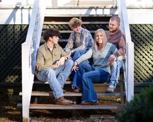 Family sitting together on outdoor white wooden stairs during casual photo session.