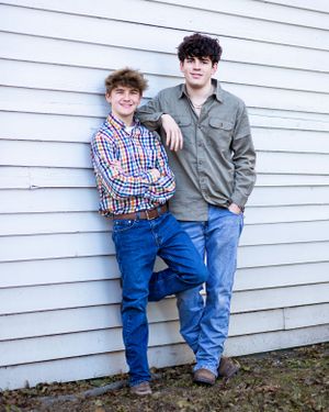 Two casually dressed people leaning against white siding of building.