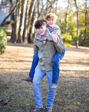 Playful outdoor portrait with one person carrying another on their back among fall trees.