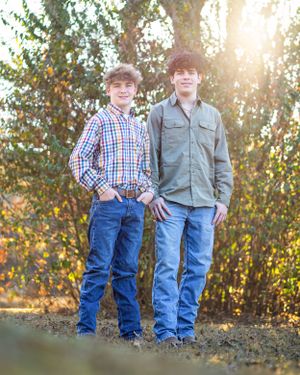 Two people standing together in casual attire against sunlit autumn foliage.