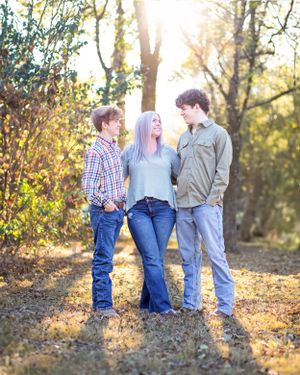 Family portrait taken in autumn forest with golden sunlight filtering through trees.