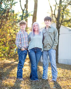 Family portrait outdoors in casual attire against autumn foliage and a white building backdrop.