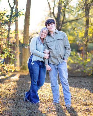 Couple embracing in front of fall trees with sunlight filtering through the branches.